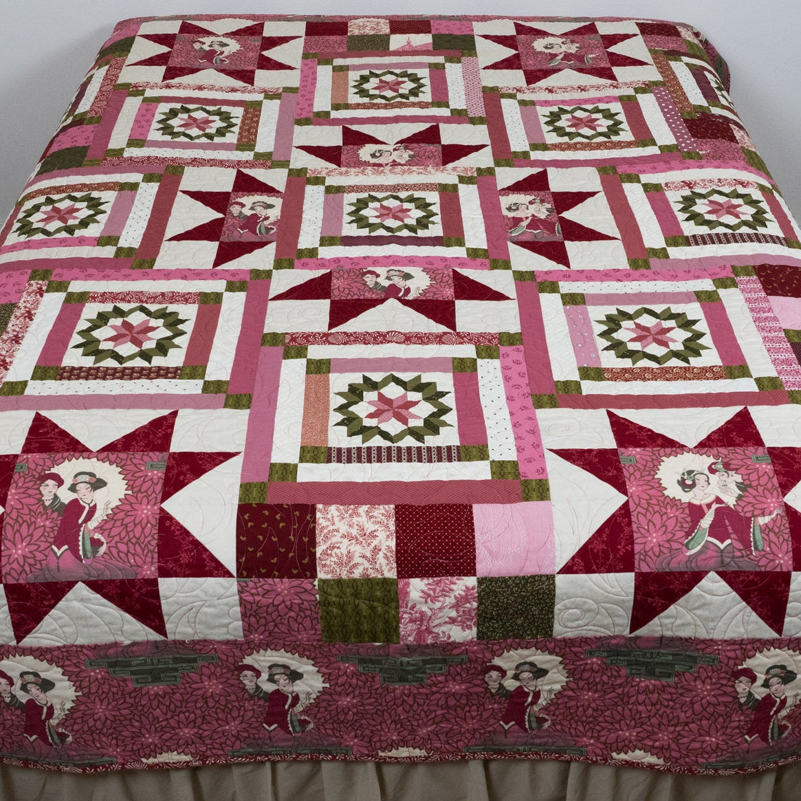 Pink geometric and star printed quilt with empress figures around the border laid out on a bed