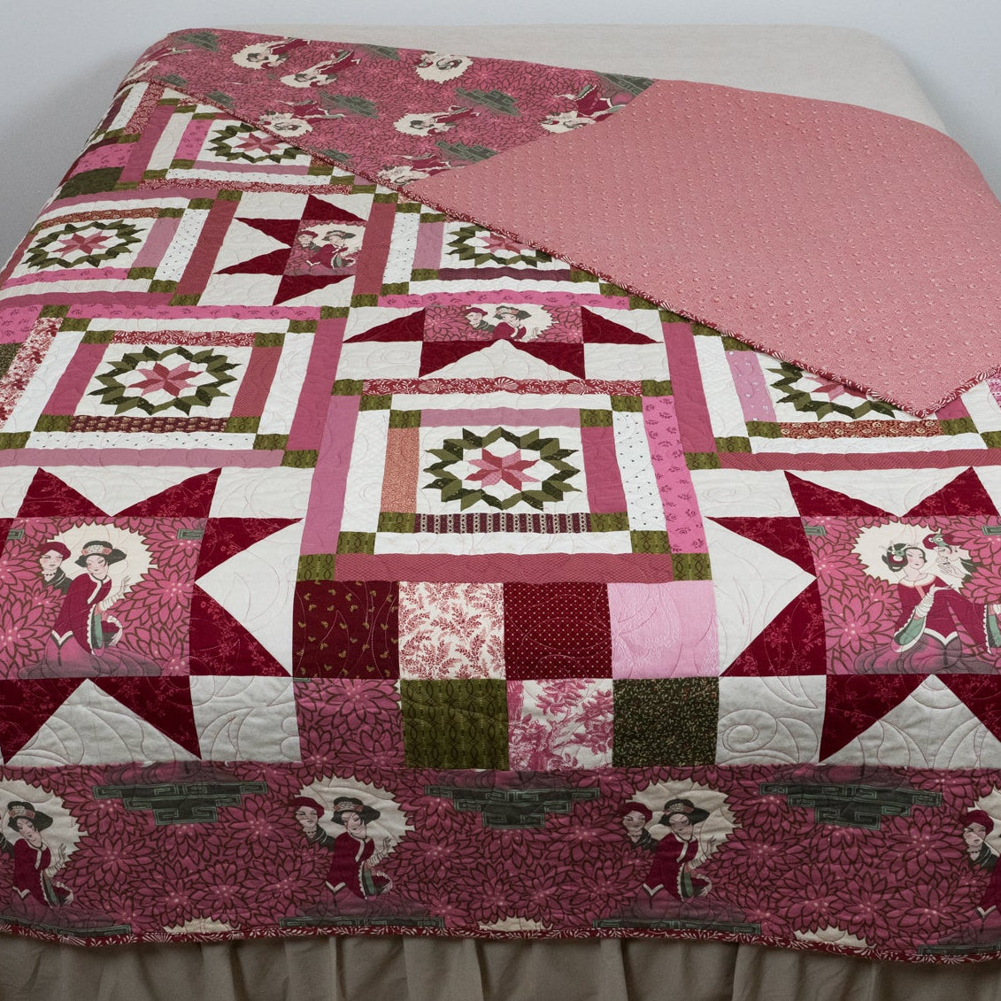 Pink geometric and star printed quilt with empress figures around the border laid out on a bed