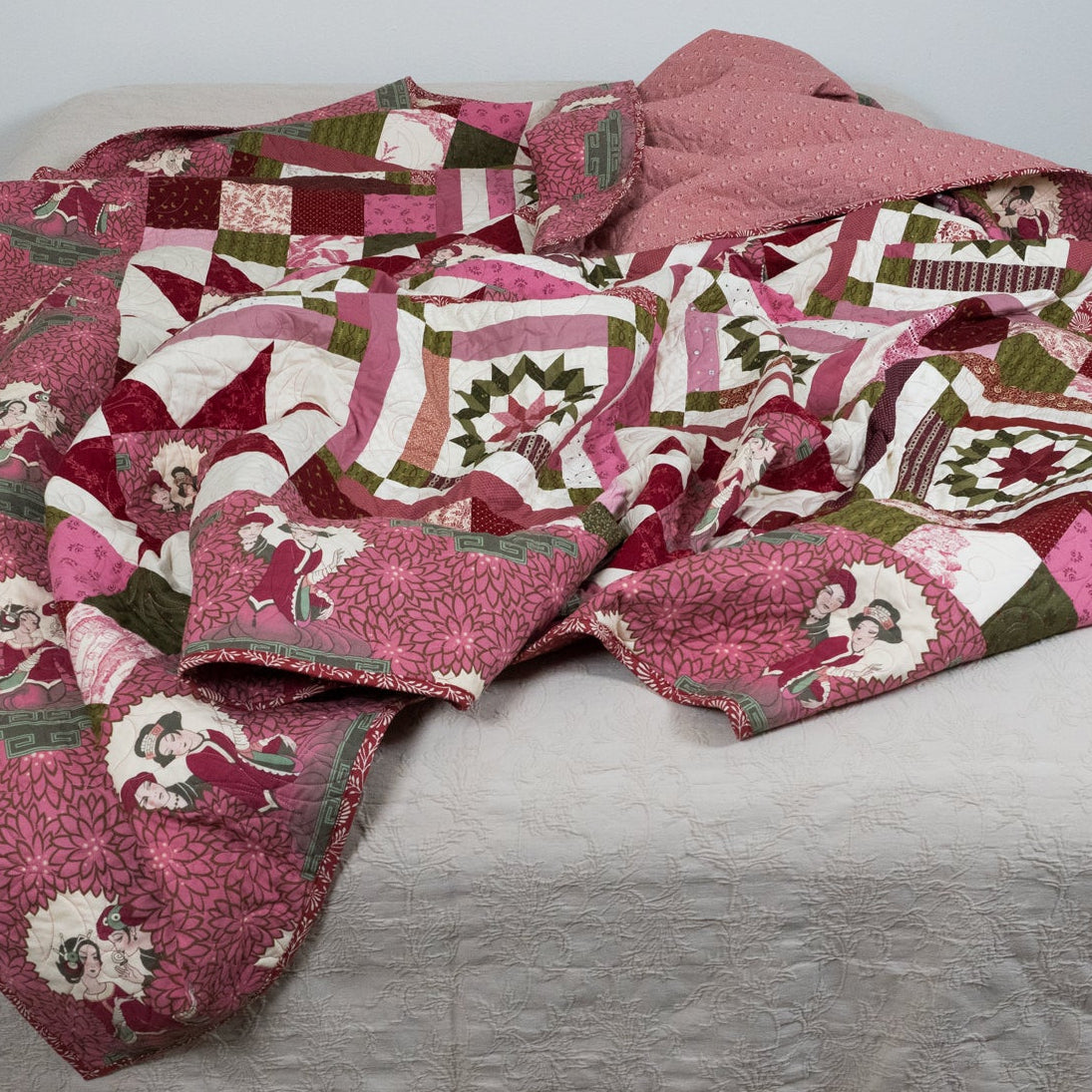 Pink geometric and star printed quilt with empress figures around the border laid out on a bed