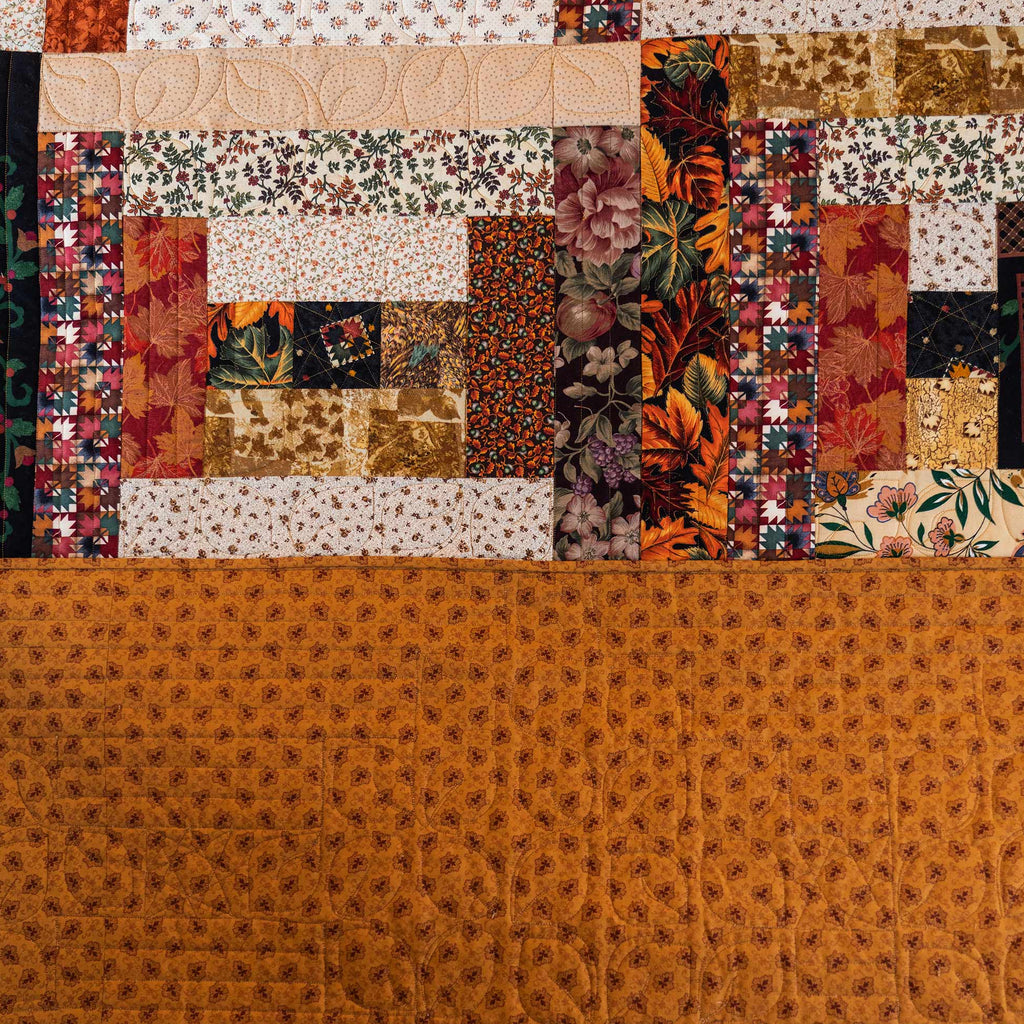 Quilt with a patchwork design featuring various patterns and colors, with a brown border.