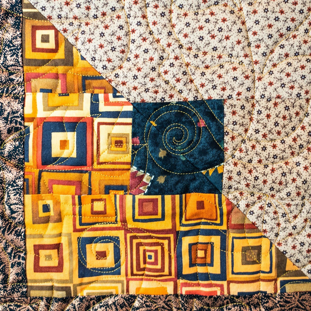 Quilt block with a leaf print and a square block print in yellow and blue tones with intricate leaf stitching. 