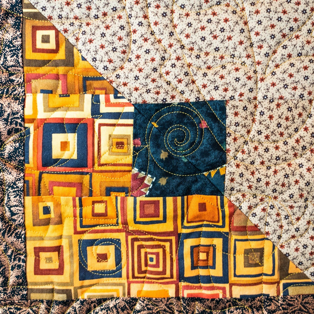Quilt block with a leaf print and a square block print in yellow and blue tones with intricate leaf stitching. 