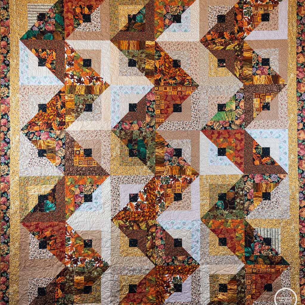 Quilt with a streak of lightening print made up of brown and orange leaf prints with a floral border.