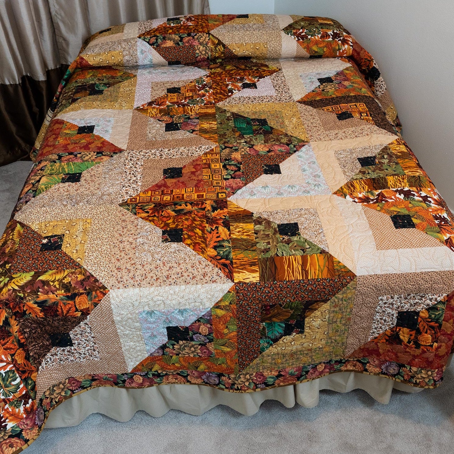 Quilt in a brown and orange leaf print in a streak of lightening layout laid out on a bed. 