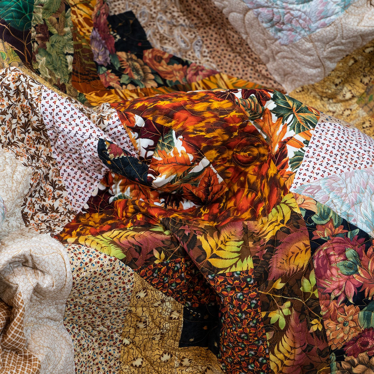 Quilt laid out with a variety of brown and orange leaf and floral prints.
