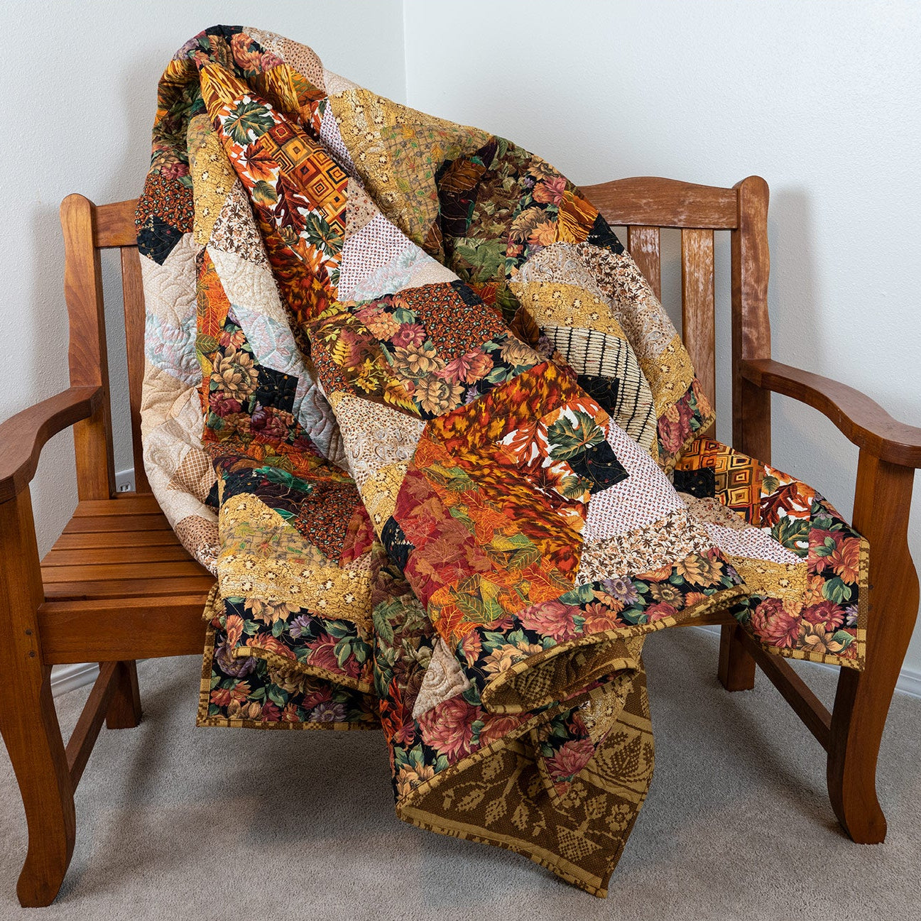 Brown and orange leaf printed quilt laid out on a wooden bench.