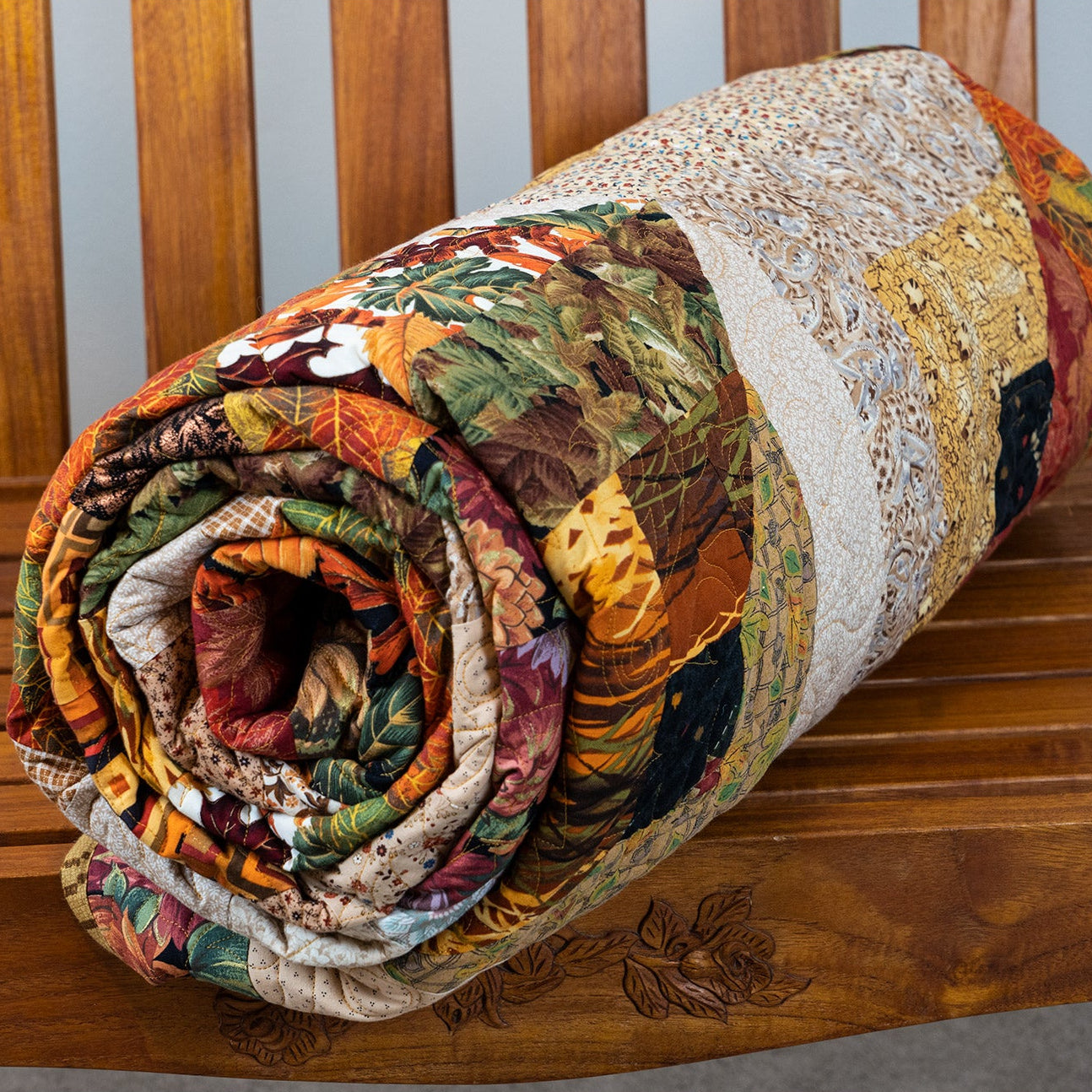Brown and orange print quilt rolled up and placed on a wooden bench.