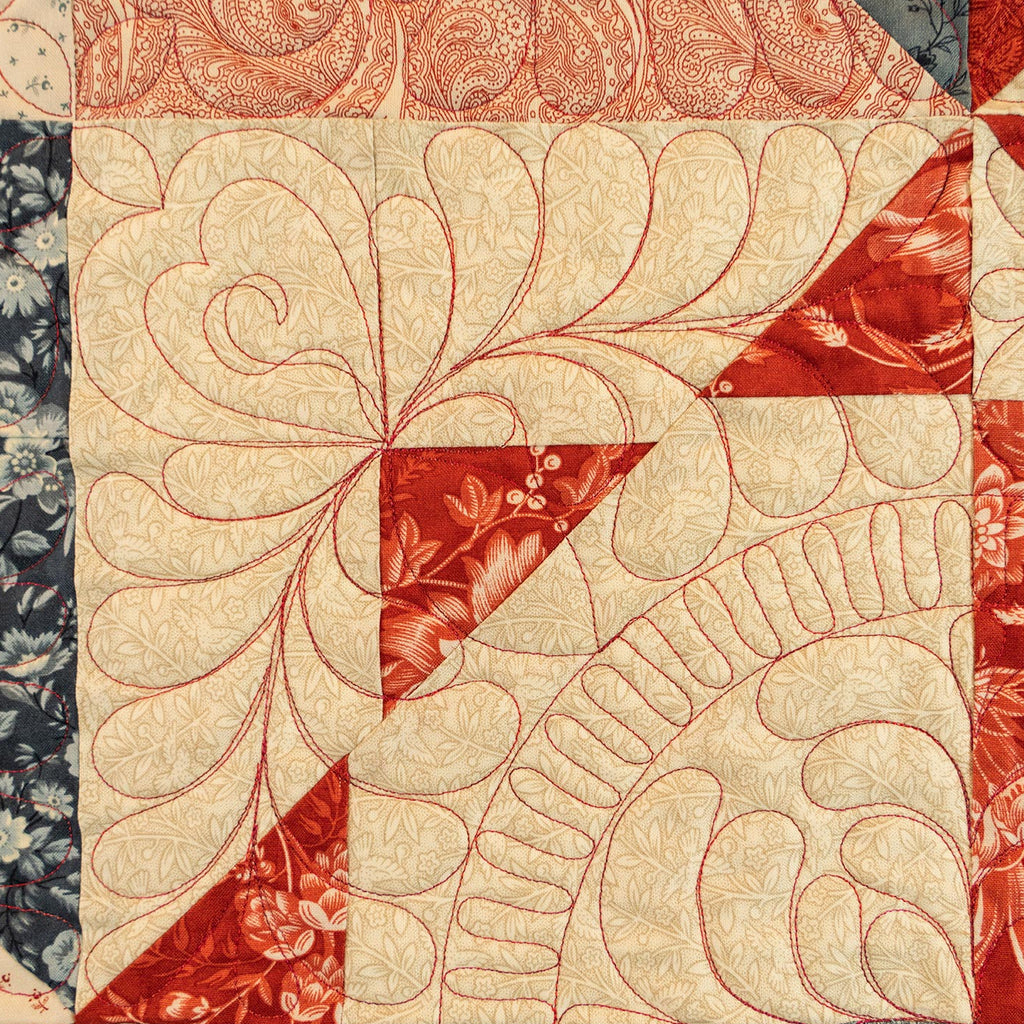 A close-up of a quilted fabric panel featuring cream and red floral patterns with detailed stitching.