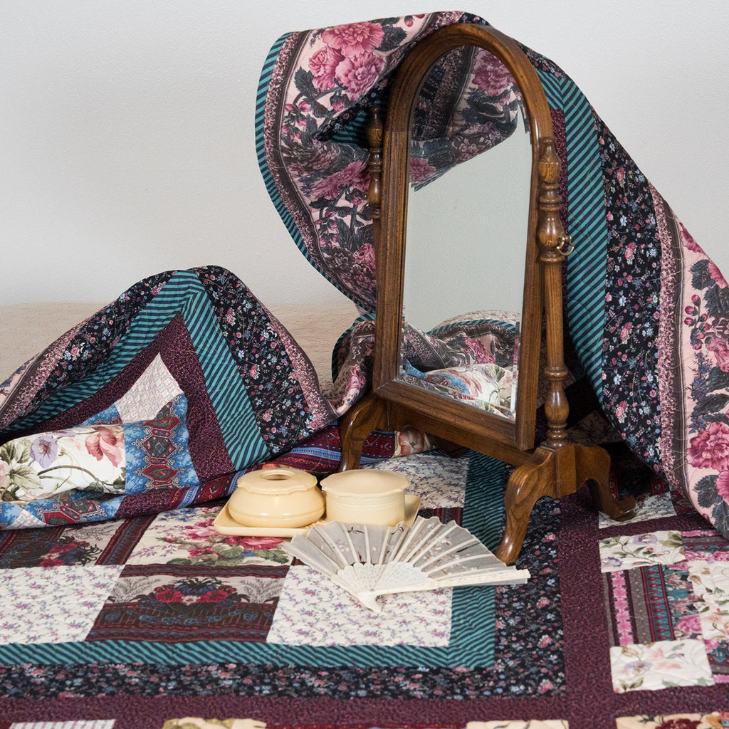Vintage patchwork quilt draped over a wooden chair with a mirror, on a plain background