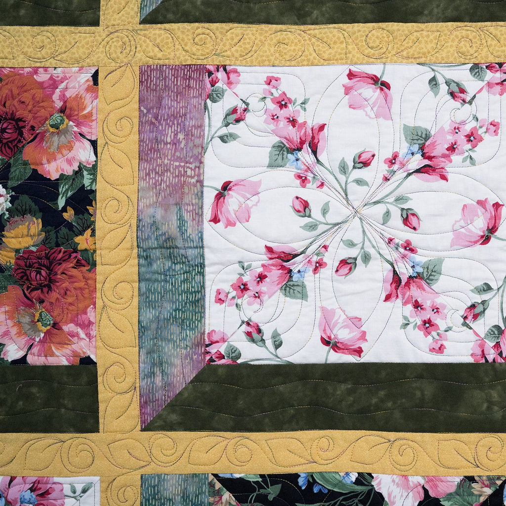 Floral quilt with a decorative gold frame surrounded by other floral patterns.