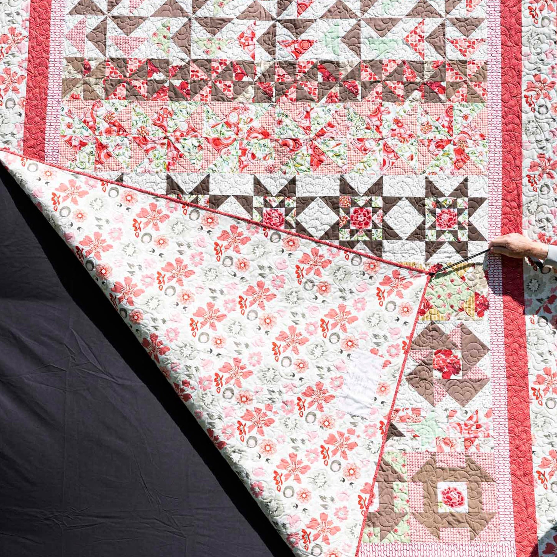 Quilt with floral and geometric patterns held by a person against a dark background