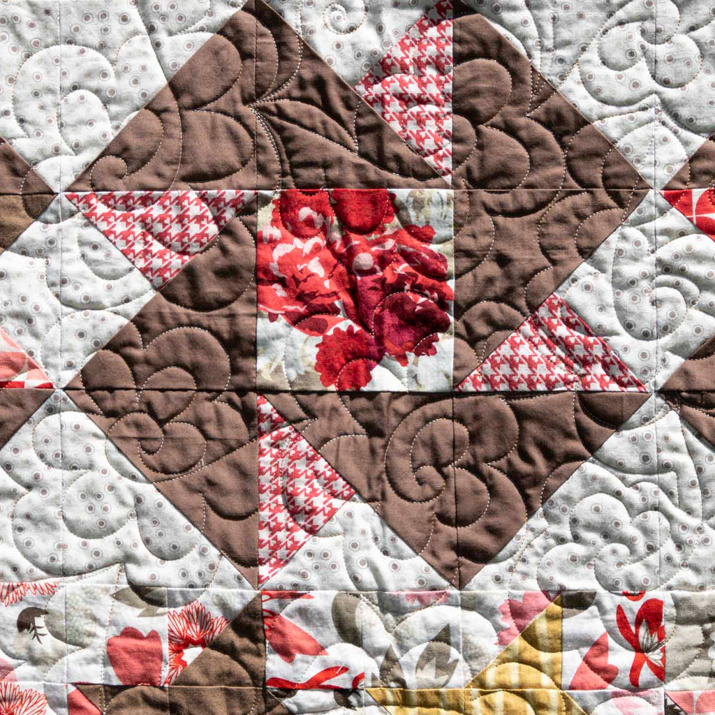 Quilt with a patchwork pattern featuring triangles in brown, white, and red.