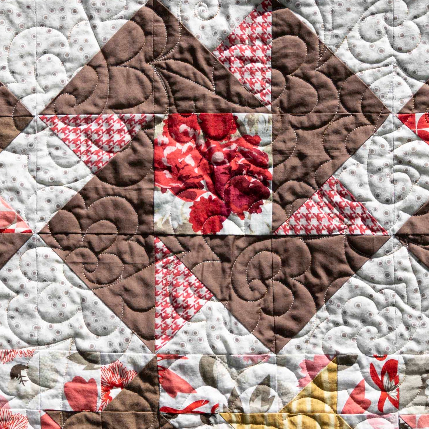 Quilt with a patchwork pattern featuring triangles in brown, white, and red.