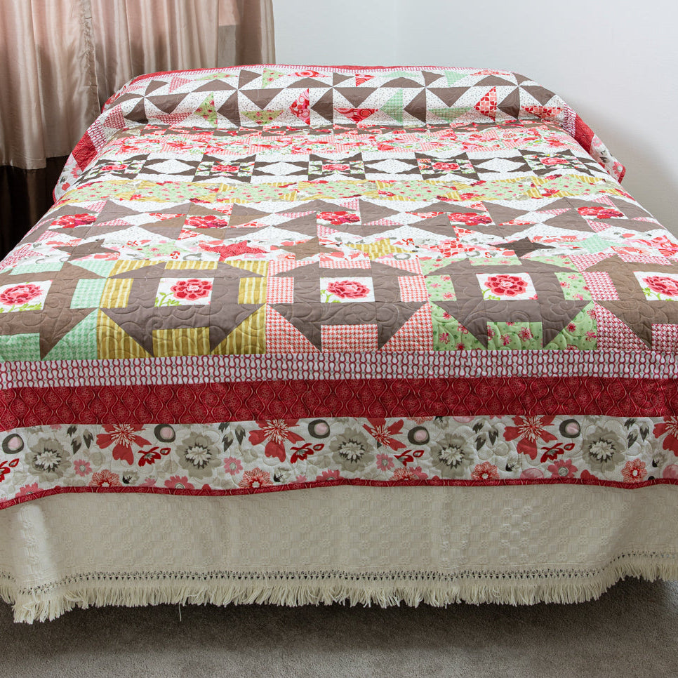 Quilt with geometric pattern on a bed in a room with curtains.