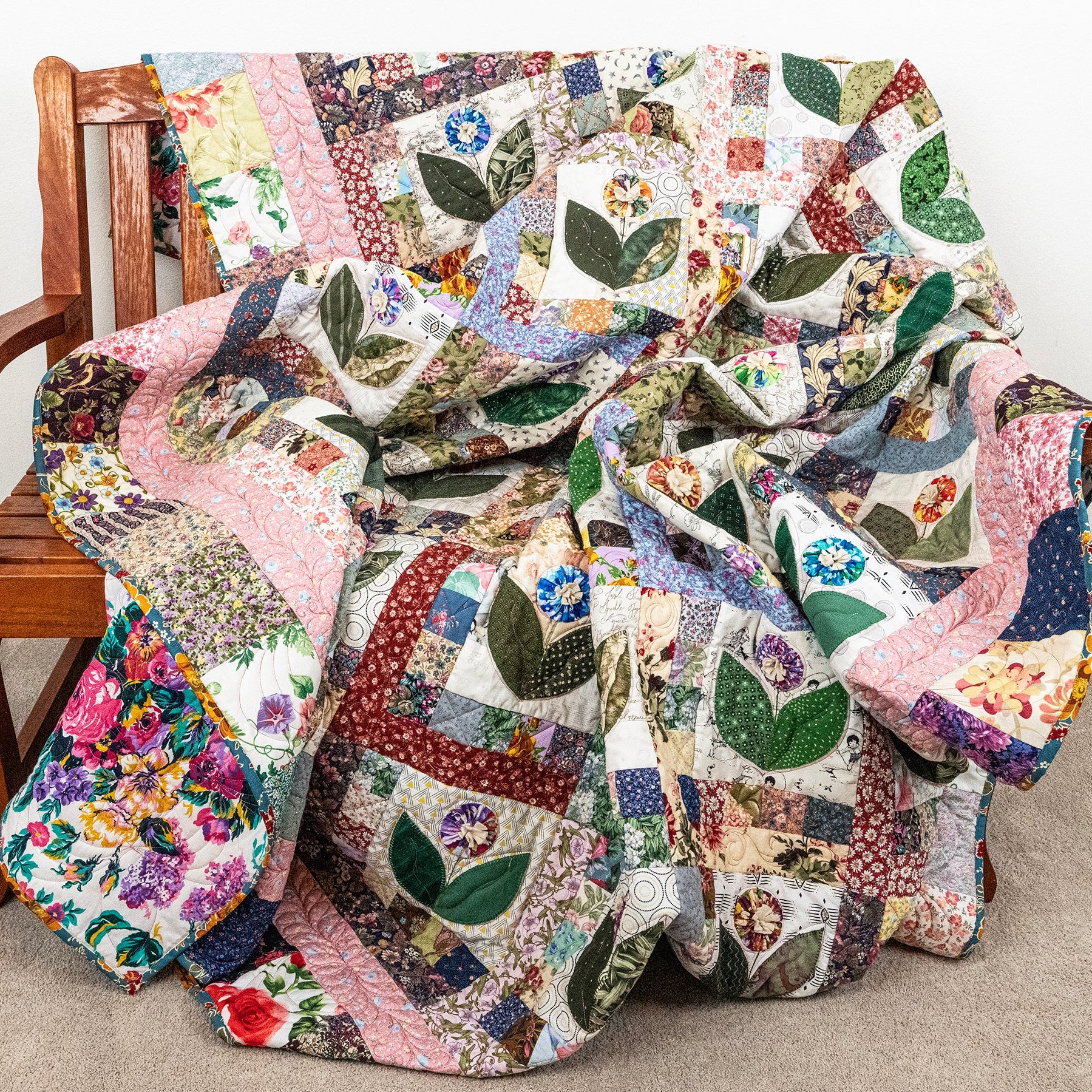 A multicolor patchwork quilt with floral and leaf motifs draped over a wooden chair in a home setting.