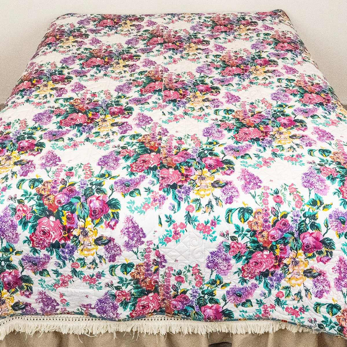 A floral quilted bedspread with a beige ruffled bed skirt, displayed on a bed in a bedroom corner.