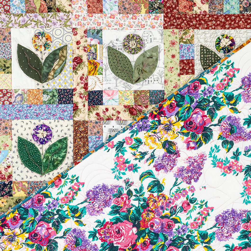 A close-up of a quilted fabric featuring a diagonal split design: one side shows a multicolor floral print with pink, purple, yellow, and green flowers on a white background, and the other side shows a patchwork quilt with floral and geometric motifs.