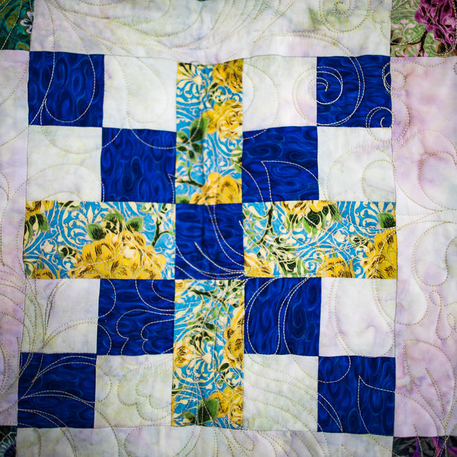 Quilt with a patchwork pattern featuring blue, yellow, and green squares on a white background.