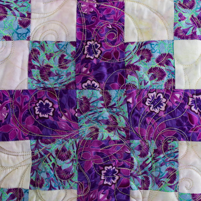 Patchwork quilt with floral patterns in purple, green, and white.