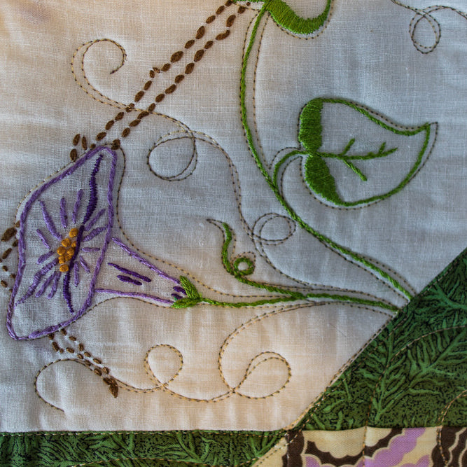 Close up quilt detail on embroidered leaves and flowers in purple and green on a white base