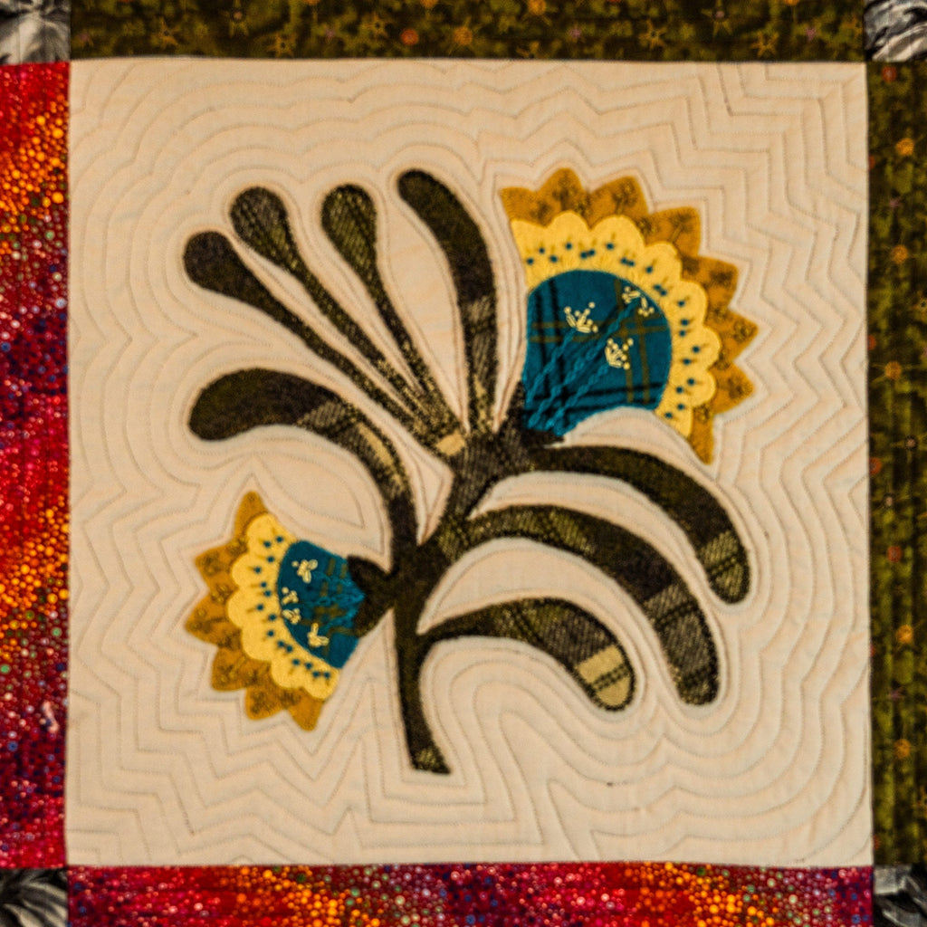 Quilt block with floral design featuring black, yellow, and blue on a beige background.
