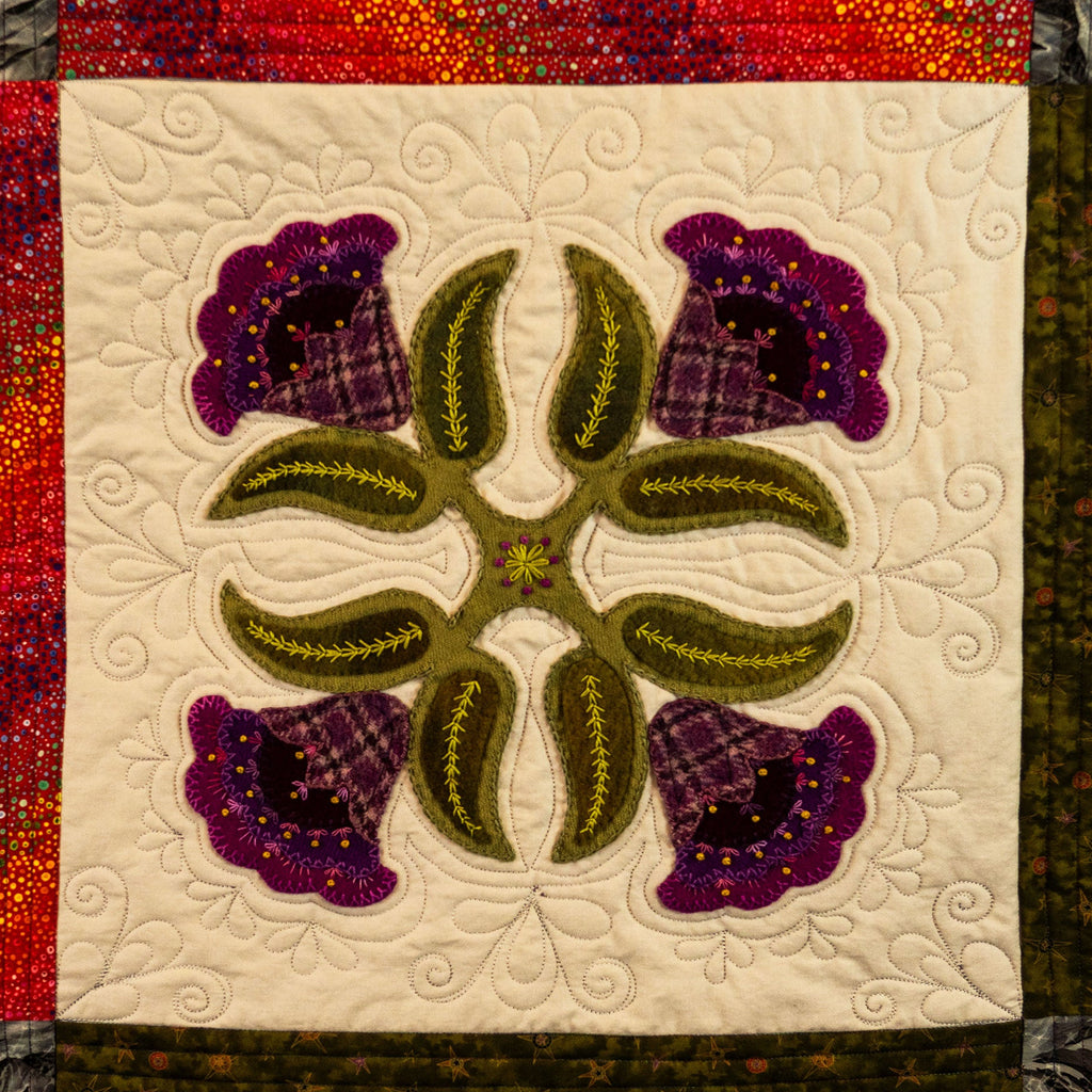 Quilt block with floral design featuring purple flowers and green leaves on a white background.