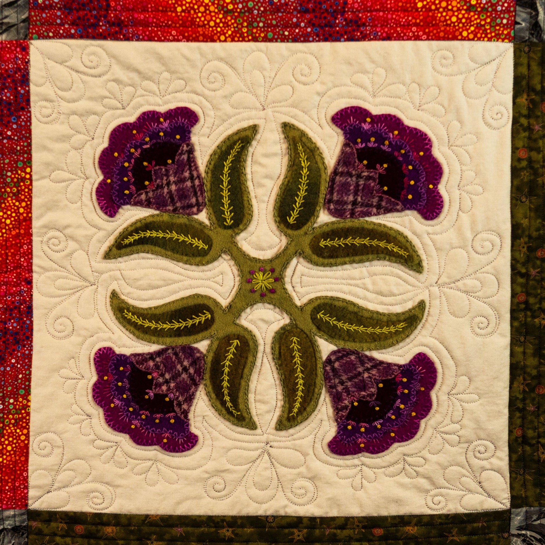 Quilt block with floral design featuring purple flowers and green leaves on a white background.
