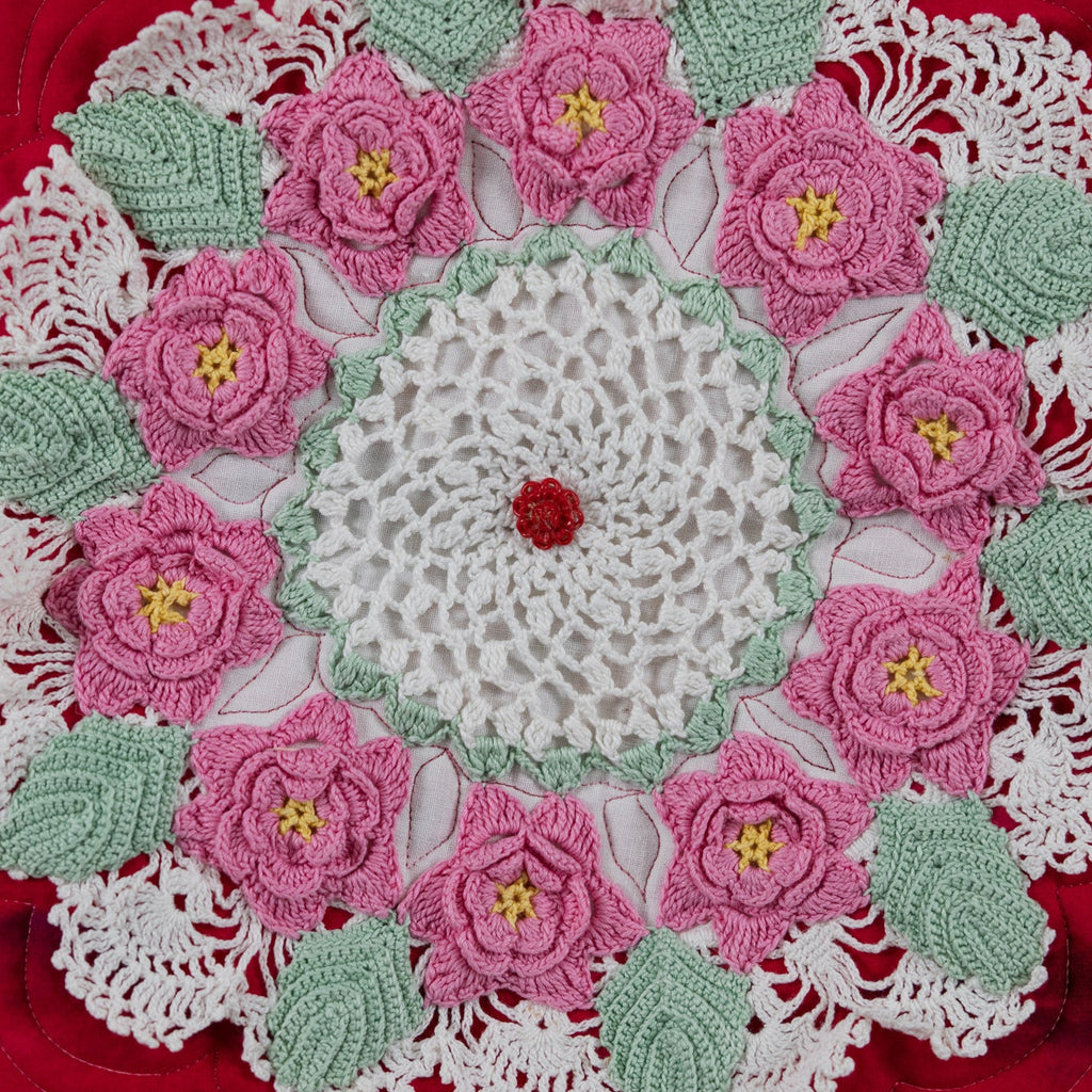 Crocheted doily with pink flowers and green leaves on a red surface