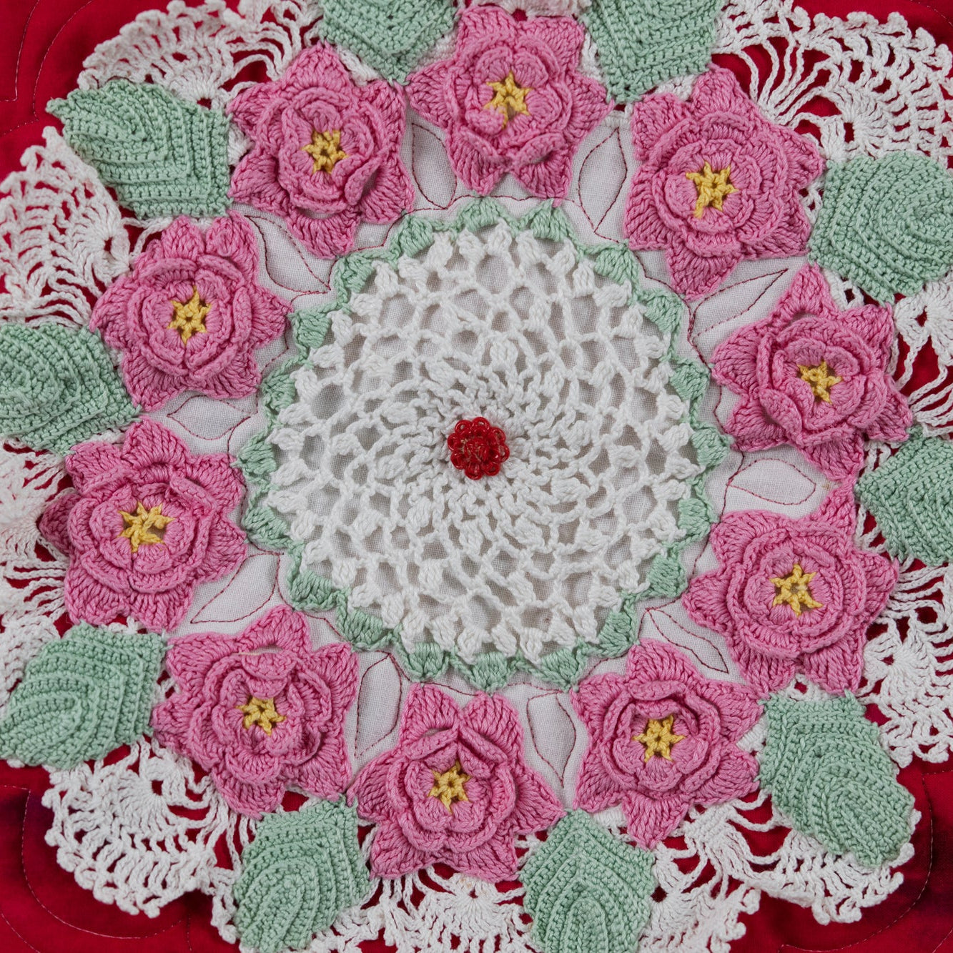 Crocheted doily with pink flowers and green leaves on a red surface