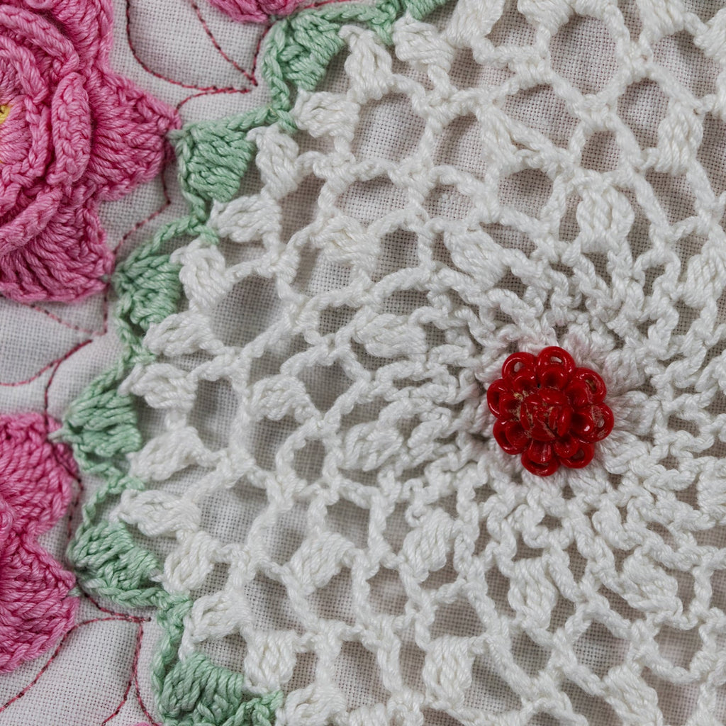 Close-up of a crocheted doily with floral patterns in pink, green, and red.