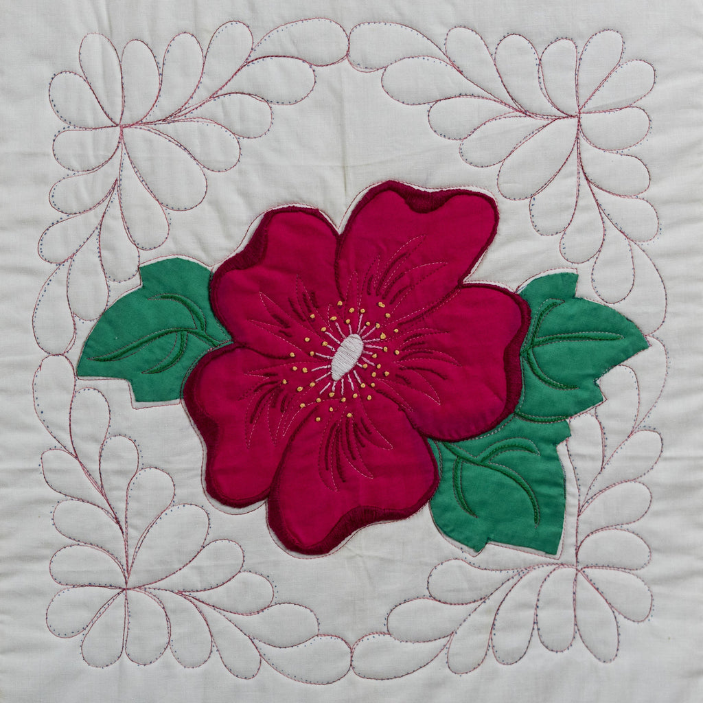 Quilt block with a red flower and green leaves on a white background
