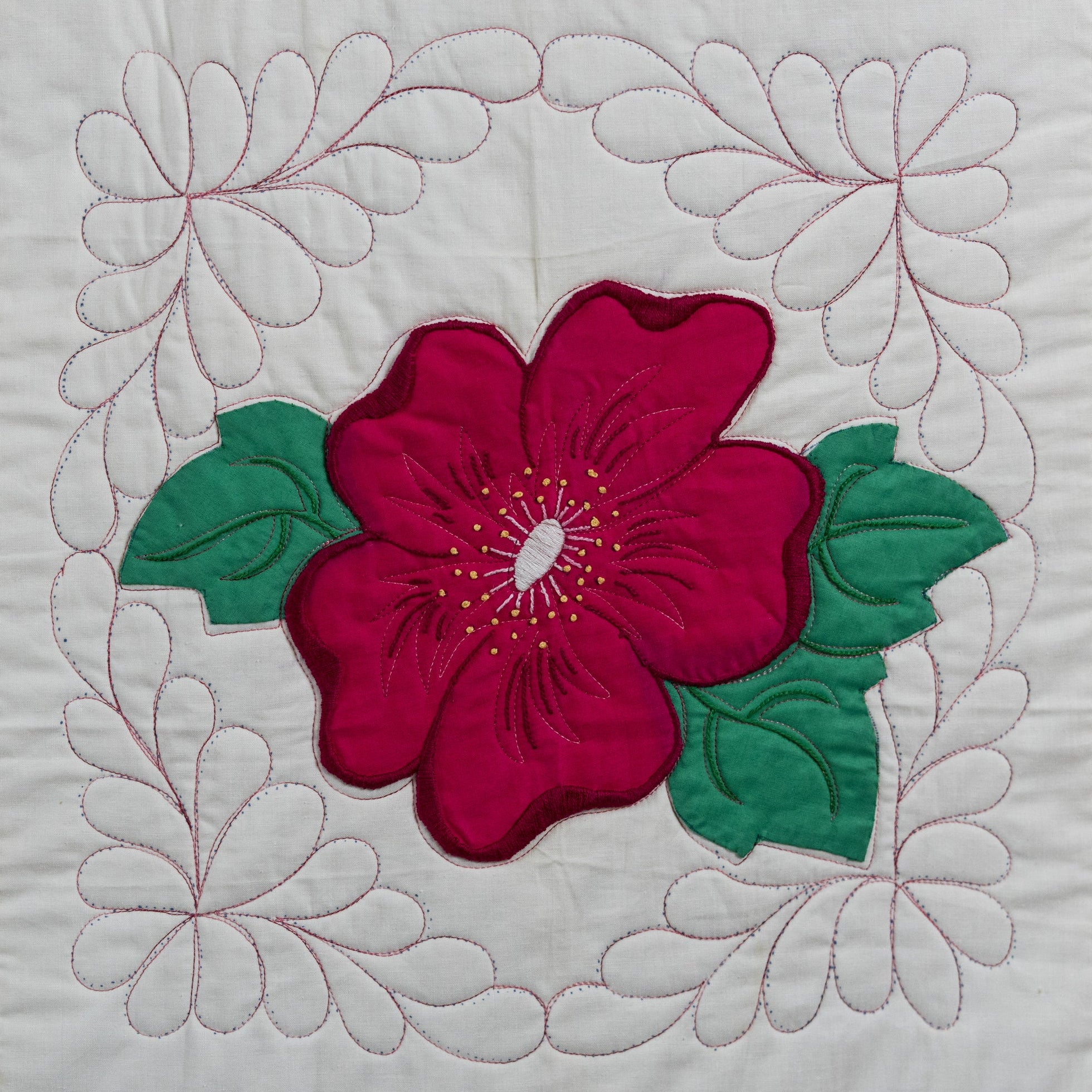 Quilt block with a red flower and green leaves on a white background