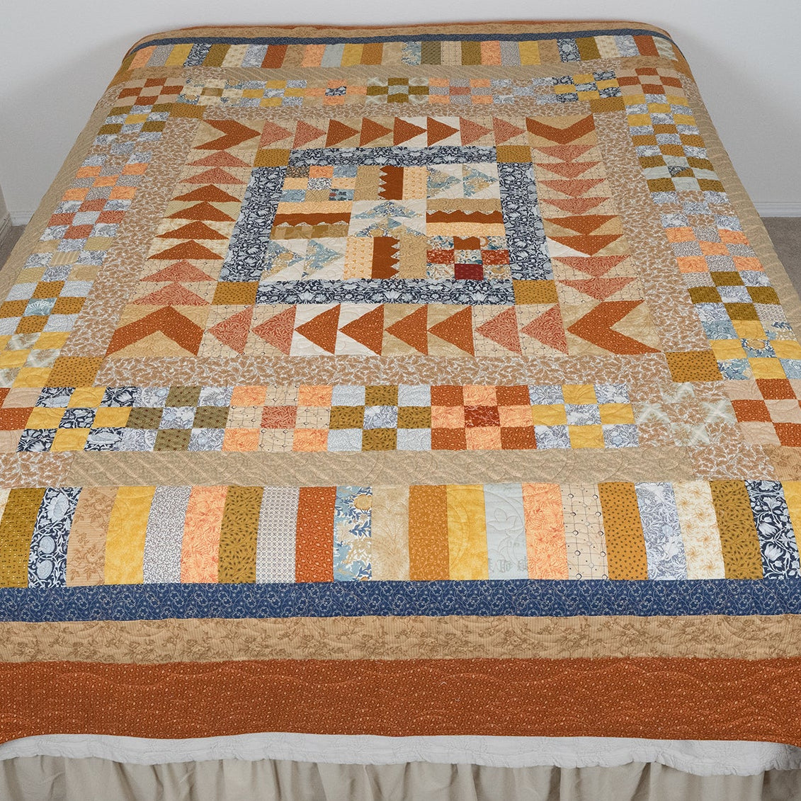 Colorful quilt with geometric patterns on a bed against a white wall.