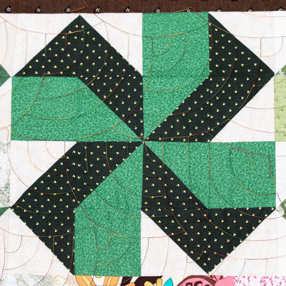 A close-up of a quilted fabric block pattern featuring a green and black pinwheel design with floral and solid patterned sections.