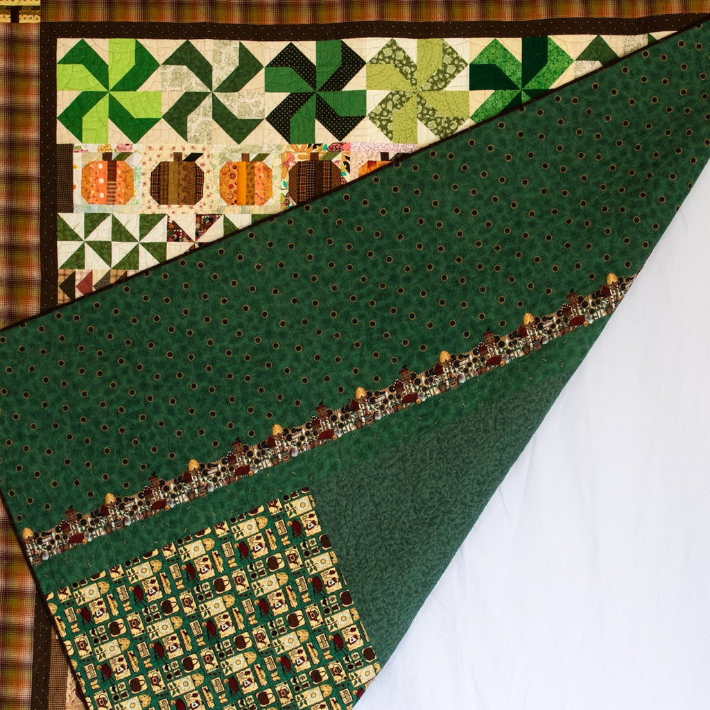 A handmade quilted blanket or throw with a green forest pattern and a pumpkin patch border, held up by a person against a white studio backdrop.