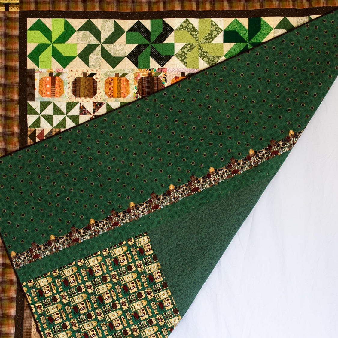 A handmade quilted blanket or throw with a green forest pattern and a pumpkin patch border, held up by a person against a white studio backdrop.