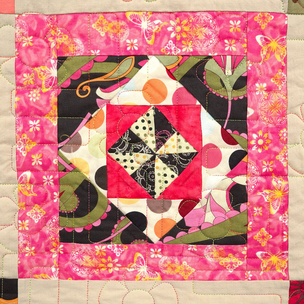 Colorful quilt with geometric patterns and floral elements on a pink background