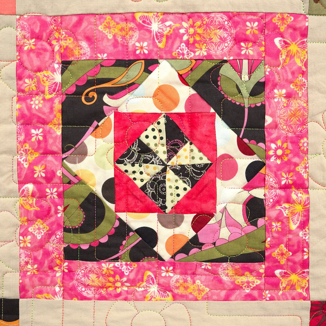 Colorful quilt with geometric patterns and floral elements on a pink background