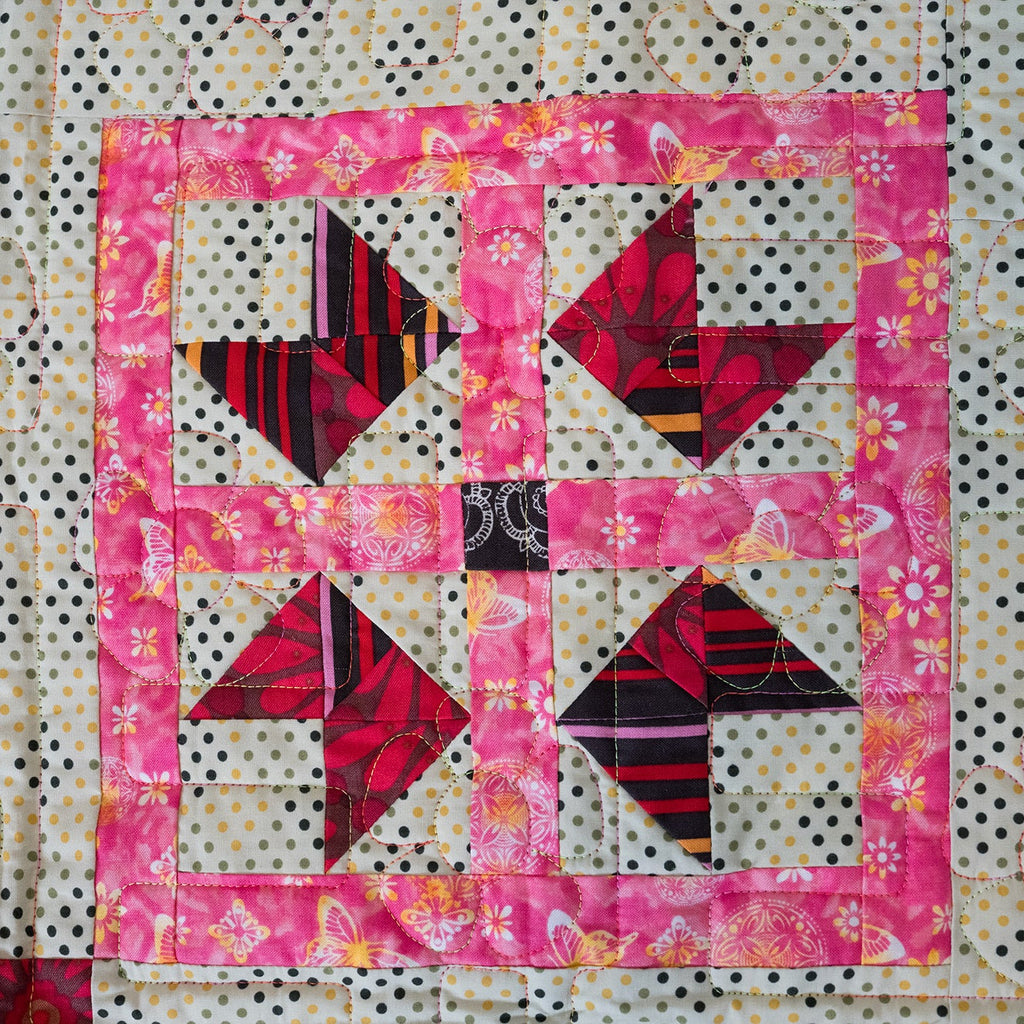 Quilt block with pink border and geometric pattern on a polka dot background