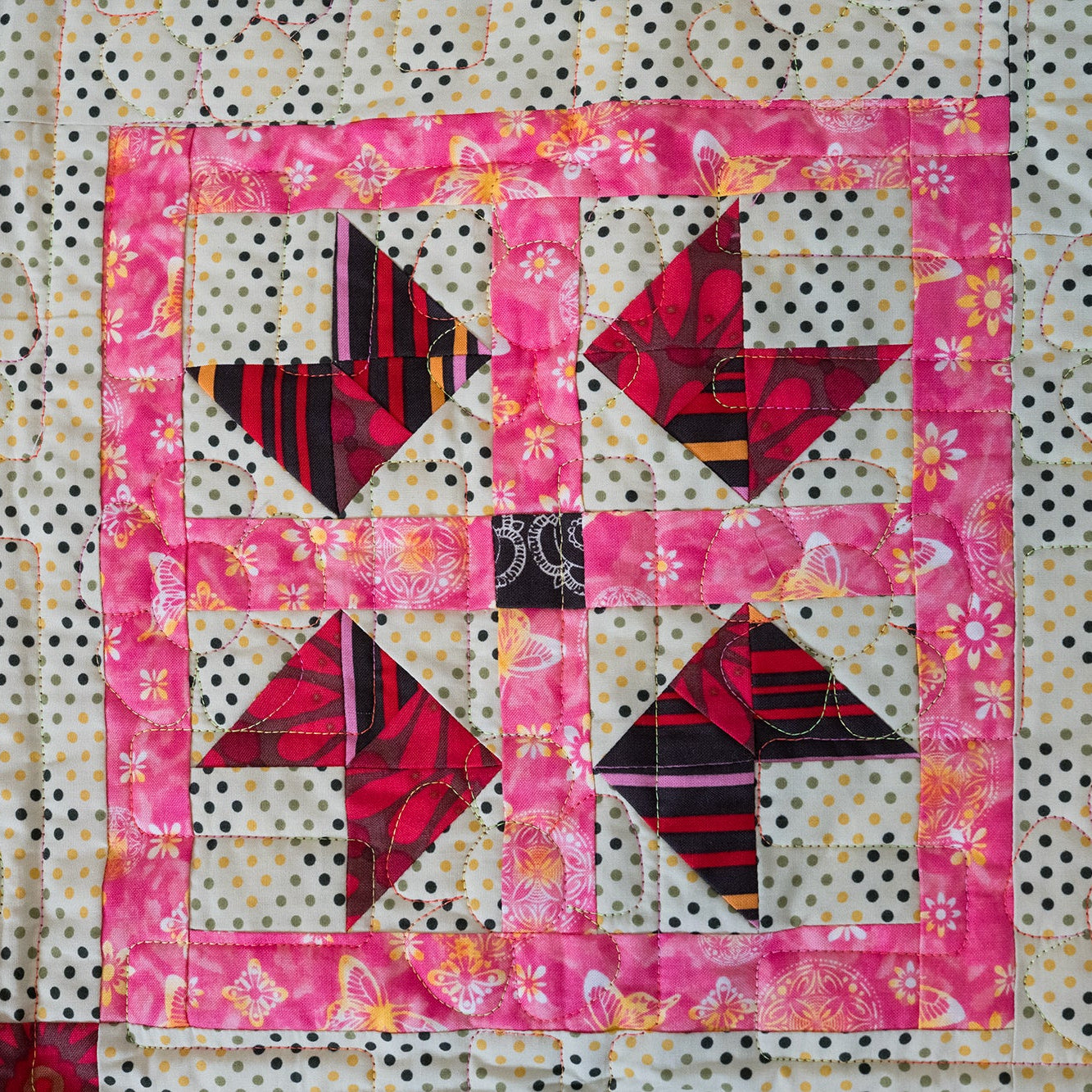 Quilt block with pink border and geometric pattern on a polka dot background