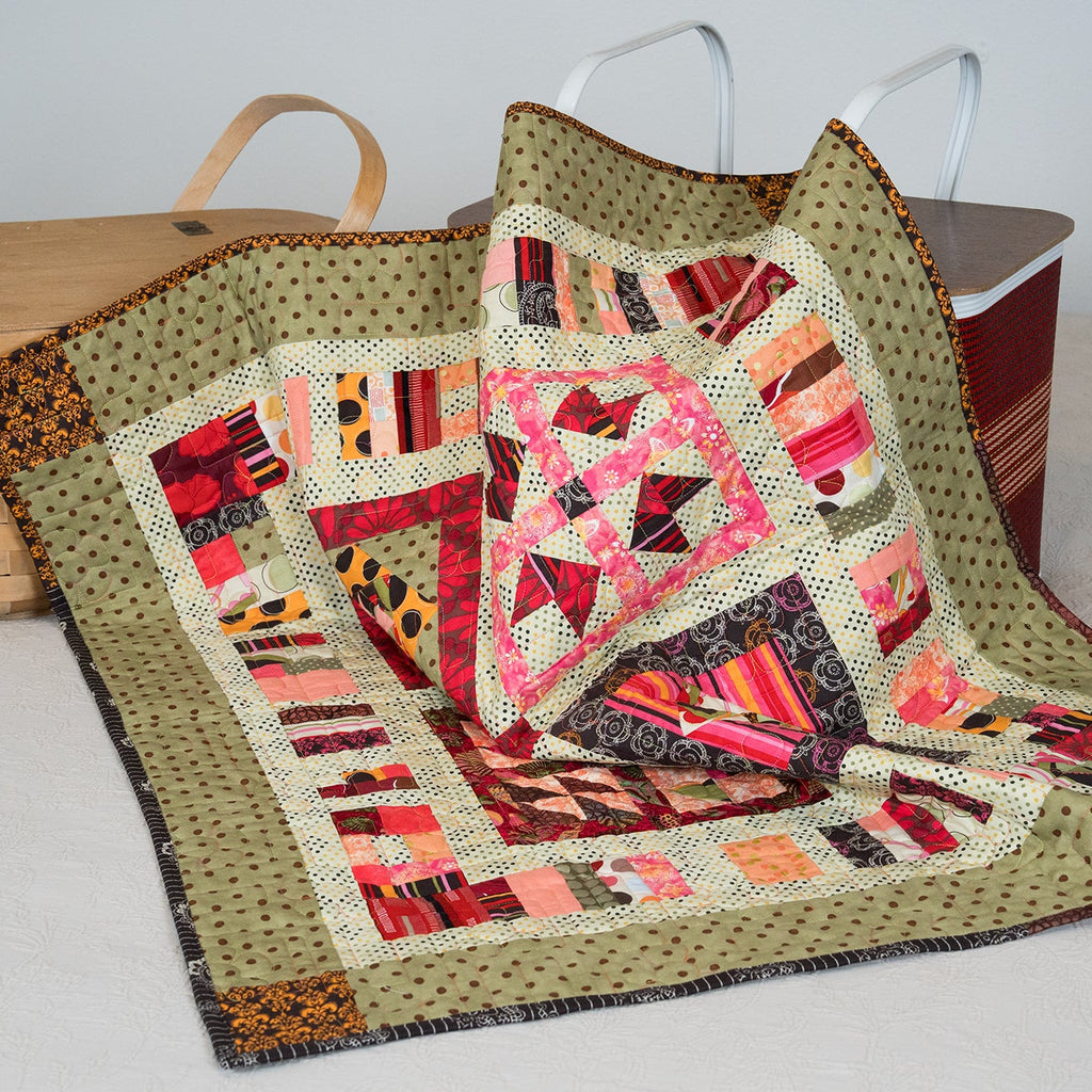 Colorful quilt with geometric pattern on a white surface, with baskets in the background.
