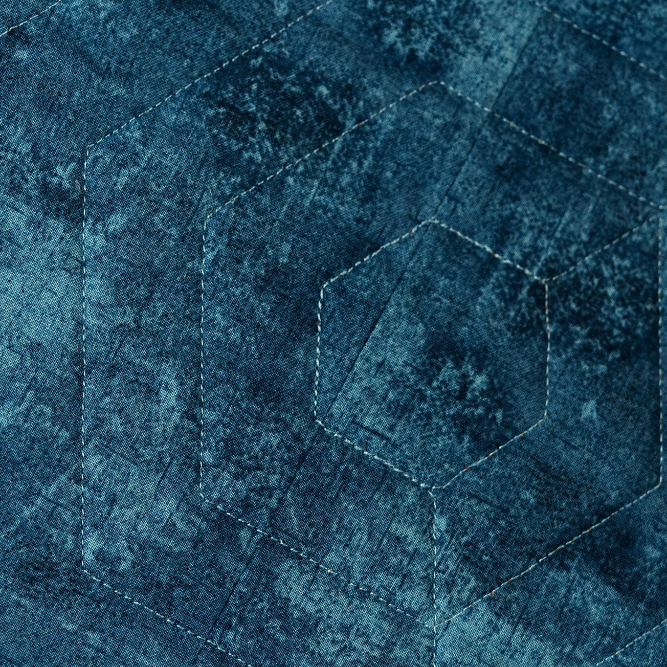 Close up of the backing of the quilt which is in a blue tone with tonal all over stitching pattern.