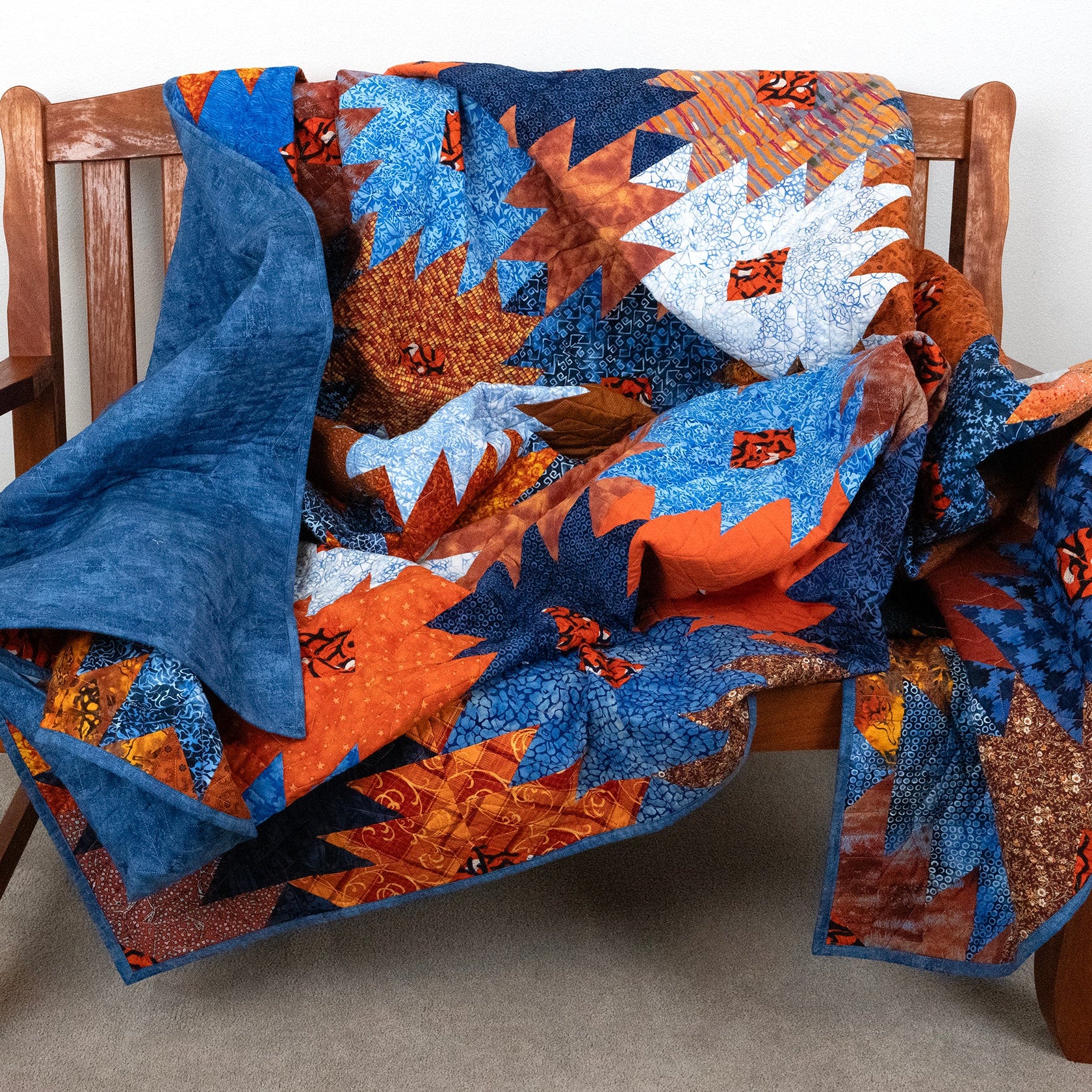 Ikat print quilt in a blue and orange honeycomb pattern laid across a wooden bench.