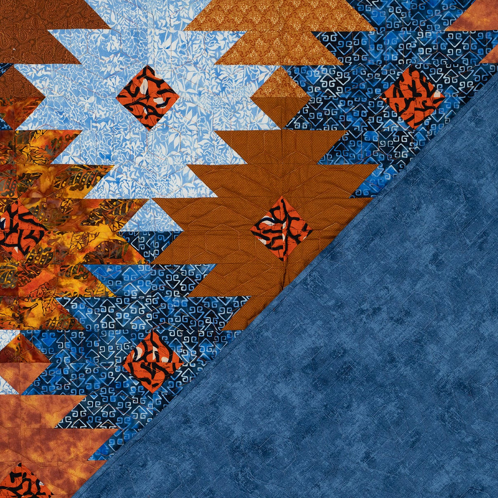 Orange and blue ikat print quilt in a honeycomb print with the backing showing in blue with tonal stitching.