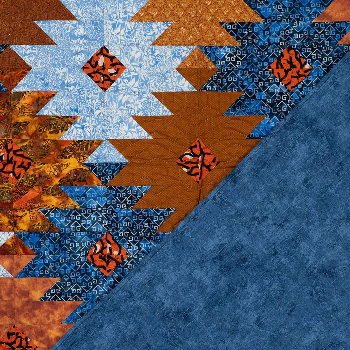 Orange and blue ikat print quilt in a honeycomb print with the backing showing in blue with tonal stitching.