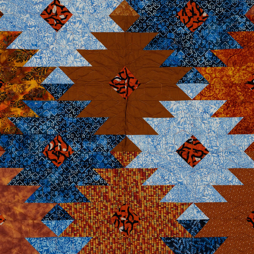 Close up of quilt with ikat print in orange and blue in a honeycomb pattern.