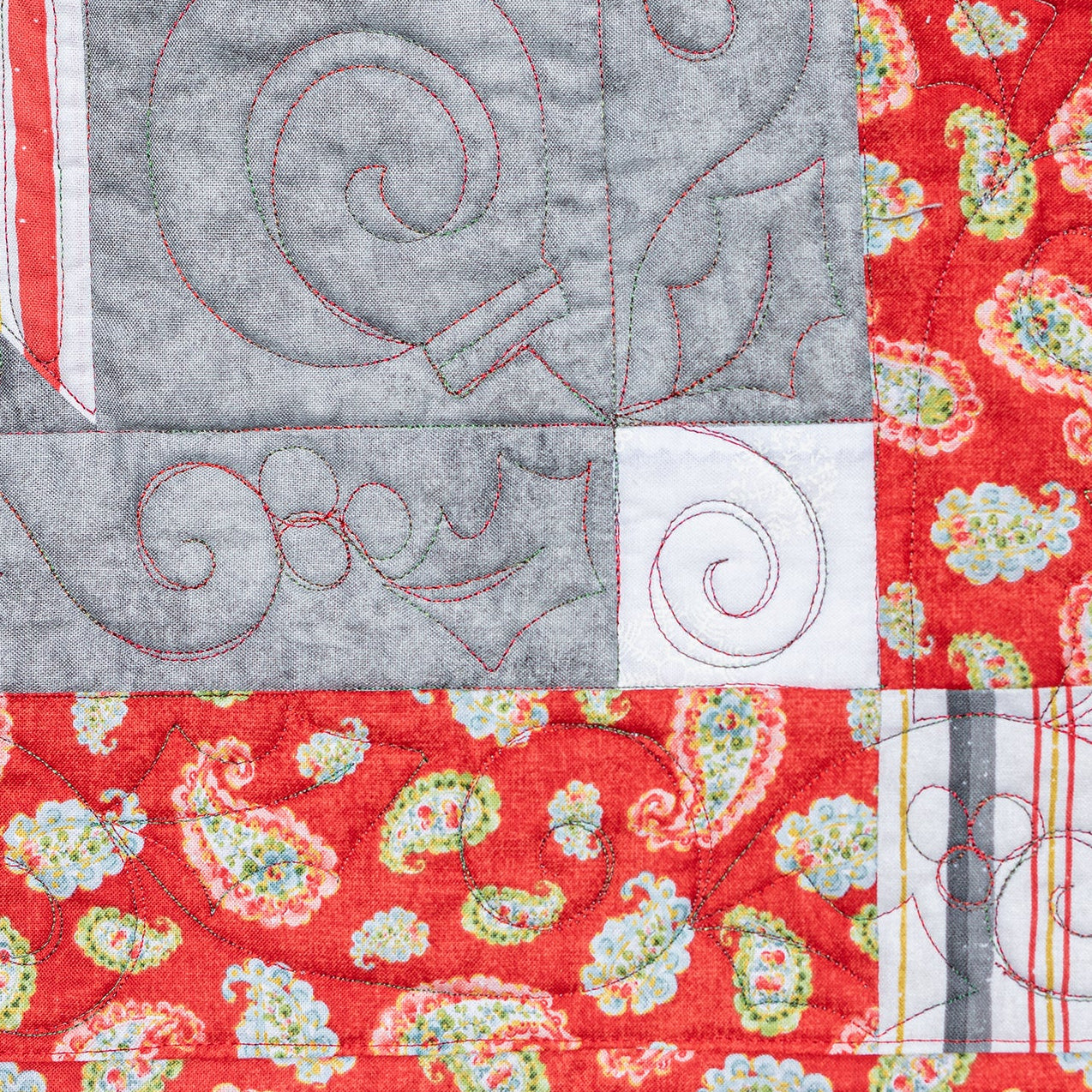 Close-up of a quilt with red, gray, and paisley patterns on a black background.