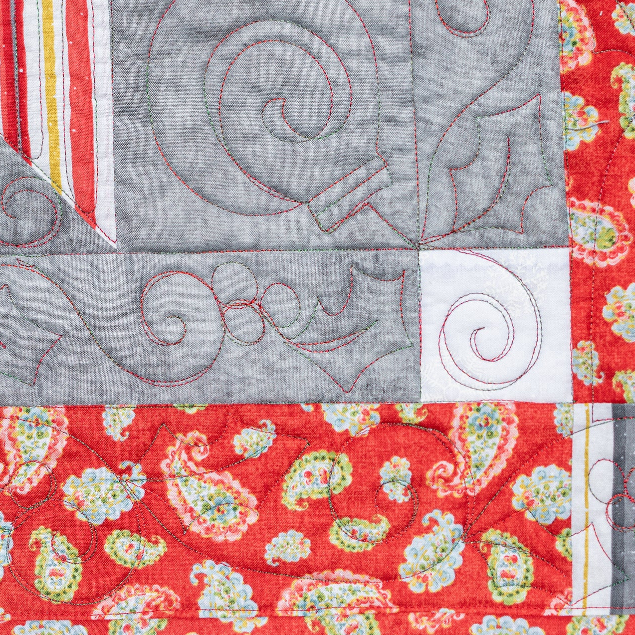 Close-up of a quilt with red, gray, and paisley patterns