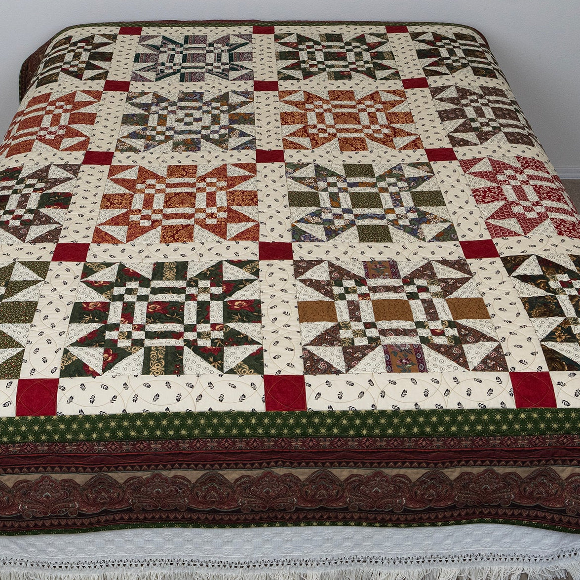 Missouri print quilt in green, orange, red and neutral tones laid out on a bed