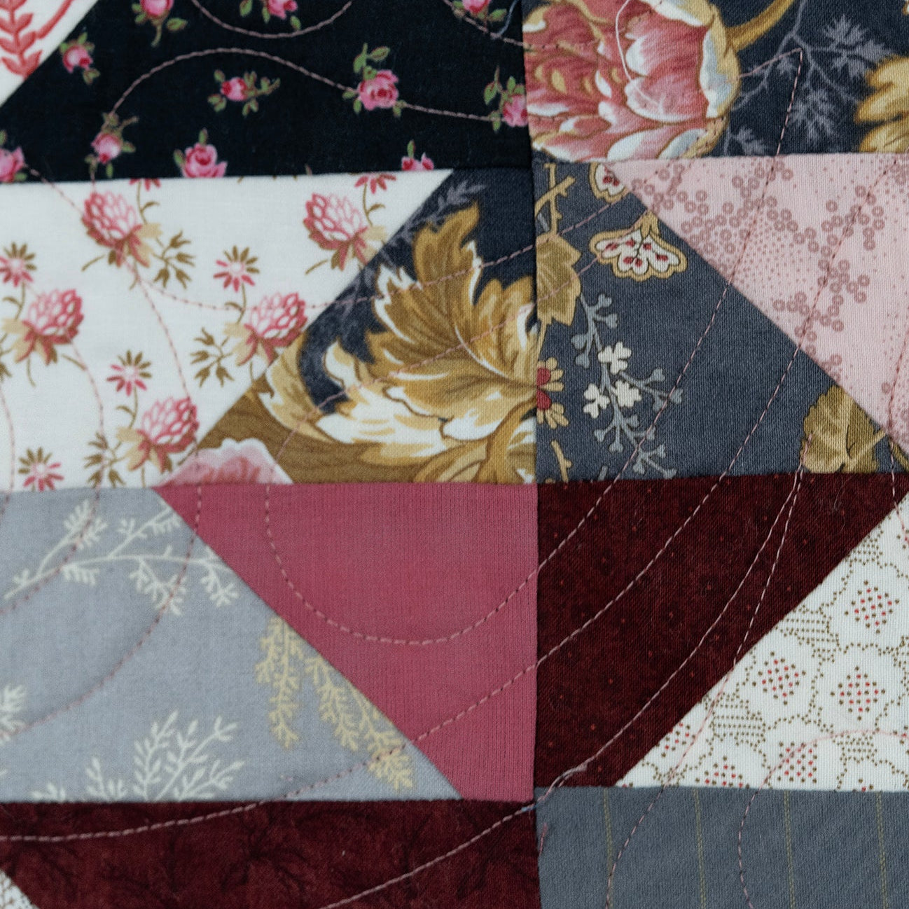 A close-up of a patchwork quilt featuring various fabric patterns and colors, including floral prints, paisley, and solid geometric sections.